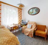 Szoba családi házban ággyal, szőnyeggel, székkel és képpel a falon.