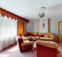 Nappali egy családi házban virágos tapétával, puha ülőgarnitúrával és hosszú függönnyel.