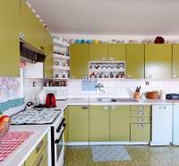 Konyha családi házban olívazöld szekrényekkel, készülékekkel és csészékkel teli polcokkal.