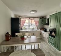 Konyha családi házban zöld konyhabútorral, étkezőasztallal és piros függönyökkel.