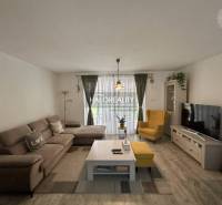 Nappali egy családi házban kanapéval, fotellel, televízióval és virágokkal.