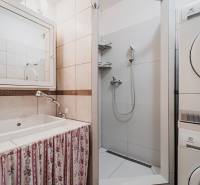 Fürdőszoba egy háromszobás lakásban mosógéppel, zuhanyzóval és függönyös mosdóval.