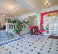 Szállodai recepció növényekkel és csillárokkal, geometriai mintás padlóburkolat.