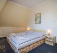 Kétszemélyes ággyal ellátott szoba, éjjeliszekrény, kép, lámpa, szőnyegek a szállodákban és panziókban.