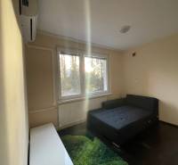 Egyszerű szoba ággyal, szőnyeggel és ablakkal egy egyszobás lakásban.