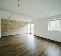 Tágas nappali kőburkolatú fallal és fa dekorációjú padlóval egy családi házban.