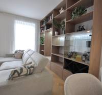 Nappali egy családi házban fehér kanapéval, fa könyvespolccal és növényekkel.