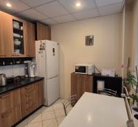 Konyha egy háromszobás lakásban fehér háztartási gépekkel, fa mintázatú padlóval és redőnyös ablakokkal.