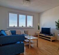 Nappali egy háromszobás lakásban kék kanapéval, televízióval és fa dekorációjú padlóval.