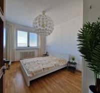 Hálószoba egy háromszobás lakásban ággyal, fehér falakkal és fa dekorációjú padlóval.