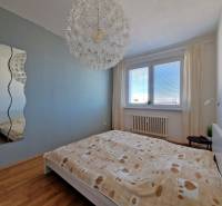 Hálószoba egy háromszobás lakásban kényelmes ággyal, tükörrel és fa dekorációjú padlóval.