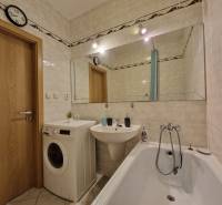 Fürdőszoba egy háromszobás lakásban káddal, mosógéppel és nagy tükörrel.