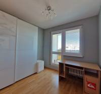 Szoba egy háromszobás lakásban, fa mintás padlóval, asztallal és szekrénnyel.