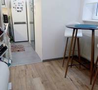 Konyha egy egyszobás lakásban fa dekorációjú padlóval, magas asztallal és székekkel.