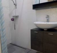 Fürdőszoba modern zuhanyzóval az egyszobás lakásban, világos csempék, mosdókagyló.