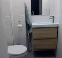 Kompakt fürdőszoba mosdóval és szekrénnyel egy egyszobás lakásban, finom textúrájú csempével.