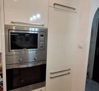 Konyha egy háromszobás lakásban fehér szekrényekkel és beépített készülékekkel.