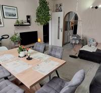 Nappali egy háromszobás lakásban kanapéval, asztallal, székekkel és gyerekhintával.