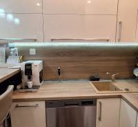 Konyha egy 3 szobás lakásban, fa dekoros padlóval, felszerelt készülékekkel és bárpulttal.