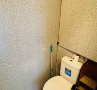 WC egy egyszobás lakásban tartállyal és dombornyomott mintás fallal.