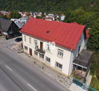 Az épület Bélán piros tetővel, környező házak és természet.