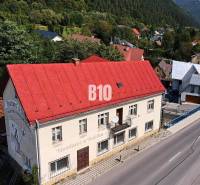 Egy piros tetős épület Bélán a főutcán, zölddel és házakkal körülvéve.