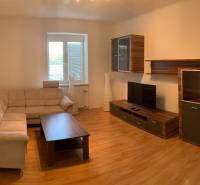 Nappali egy kétszobás lakásban kanapéval, TV-vel és fa dekoros padlóval.