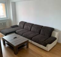 Nappali egy kétszobás lakásban sötét kanapéval és fa hatású padlóval.