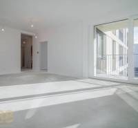 Szoba egy háromszobás lakásban nagy ablakkal, fa dekorációjú padlóval, fehér falakkal.