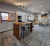 Családi ház fa dekorációjú padlóval, konyhával és nappalival, kényelmes ülőgarnitúrával.