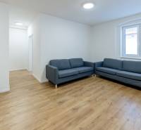 Nappali kék kanapéval és fa mintázatú padlóval egy háromszobás lakásban.