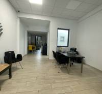 Kereskedelmi helyiségek fa mintázatú padlóval, minimalista bútorokkal és feltűnő székekkel.