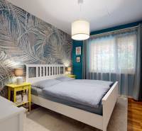 Hálószoba családi házban pálmafás tapétával, fa dekoros padlóval és fehér bútorokkal.