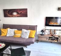 Nappali egy kétszobás lakásban kanapéval, polccal és elektromos kandallóval.