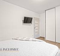 Hálószoba családi házban fehér szekrényekkel, falra szerelt TV-vel és fa dekorációjú padlóval.