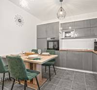 Konyha egy családi házban szürke konyhabútorral, étkezőasztallal és zöld székekkel.
