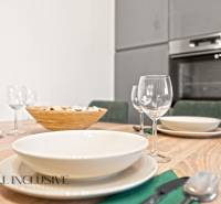 Étkezőasztal terítékkel és poharakkal, a háttérben egy családi ház konyhája.