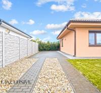 Családi ház Bősön, szilárd burkolatú bejárati úttal, kőkerítéssel és gondozott gyepfelülettel.