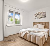 Hálószoba világos ágykerettel, fa hatású padlóval és fali képpel egy családi házban.