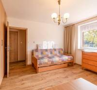 Szoba egy családi házban, fa mintázatú padlóval, kanapéval és komóddal.