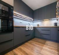 Konyha egy háromszobás lakásban sötét szekrényekkel és fa dekorációjú padlóval.