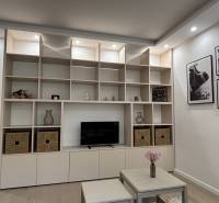 Tárolófal polcokkal és dekorációkkal egy kétszobás lakásban, mellette egy asztal virágokkal.