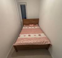 Keskeny hálószoba egy kétszobás lakásban, fa ággyal és virágos takaróval.