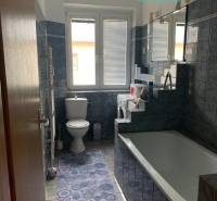 Fürdőszoba egy kétszobás lakásban káddal, mosógéppel és sötét csempékkel.