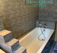 Fürdőszoba lépcsőkkel és káddal, szürke csempékkel körülvéve egy kétszobás lakásban.