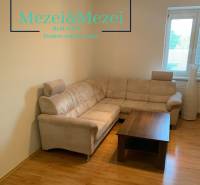 Nappali egy kétszobás lakásban sarokkanapéval és asztallal, fa dekorációjú padlón.