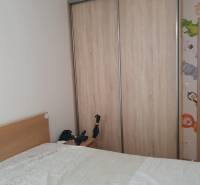 Hálószoba egy kétszobás lakásban, tolóajtós szekrény, ágy takaróval és éjjeliszekrény.