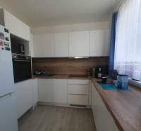 Konyha fehér szekrényekkel, fa dekorációval a padlón és munkalapon egy kétszobás lakásban.