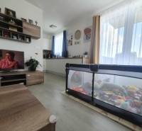 Világos nappali szoba fa mintázatú padlóval és játékokkal teli járóka egy kétszobás lakásban.