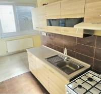 Konyha egy kétszobás lakásban fehér szekrényekkel és fa mintázatú padlóval.